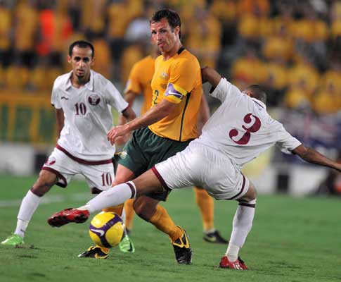 Lucas Neill (Austrália) entre dois jogadores do Qatar