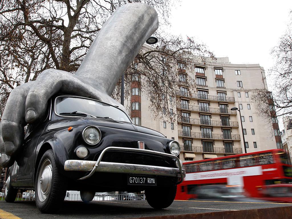 Um Fiat 500 agarrado por uma mão de alumínio é visto na escultura do artista italiano Lorenzo Quinn Vroom Vroom em Londres  (REUTERS)