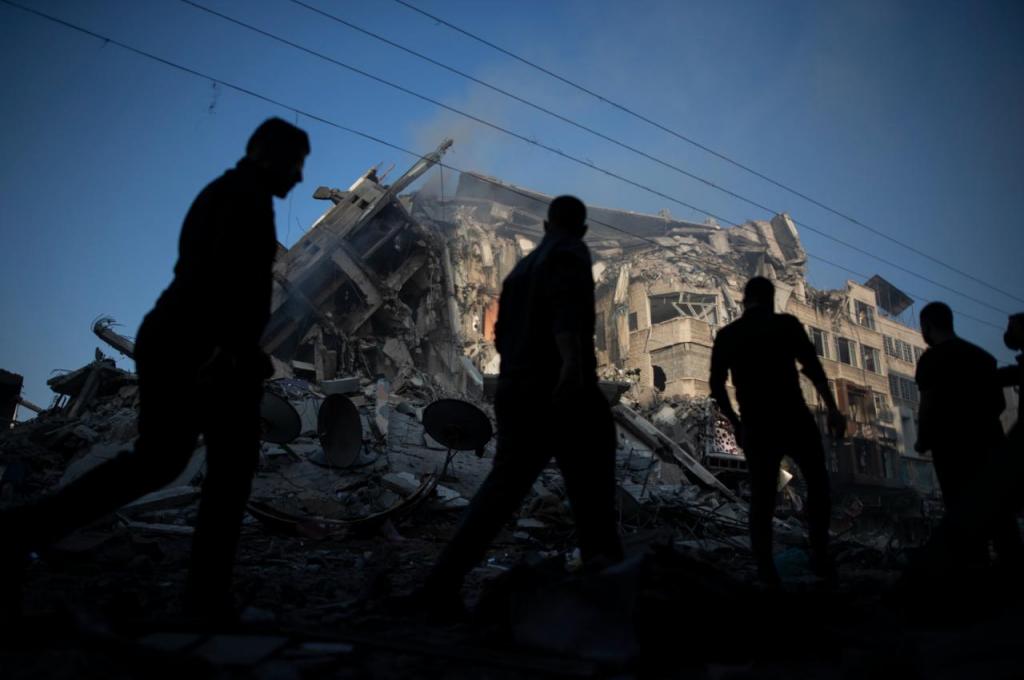 13 de maio, palestinianos passam junto a prédio de 15 andares destruído por ataques aéreos israelitas na Cidade de Gaza (Khalil Hamra, AP)