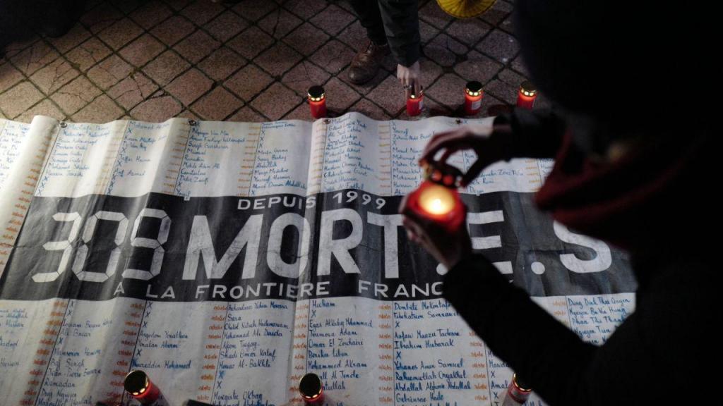 Ativistas e membros de associações de defesa dos direitos dos migrantes acendem velas em frente a uma faixa que diz 