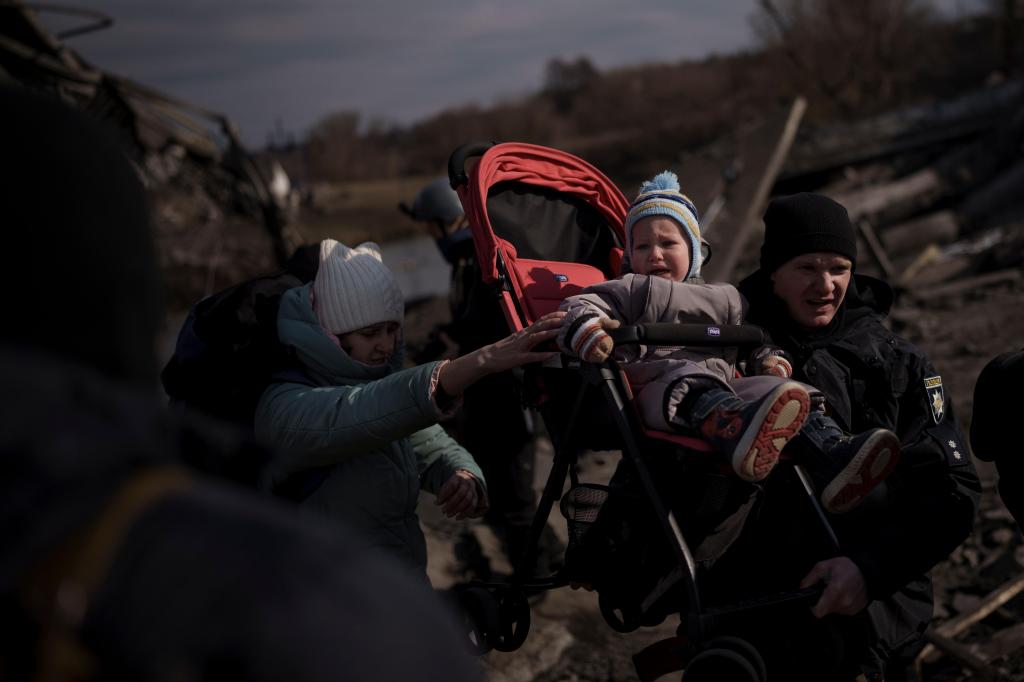 Uma criança é carregada num carrinho por um caminho improvisado enquanto foge de Irpin, nos arredores de Kiev (AP)