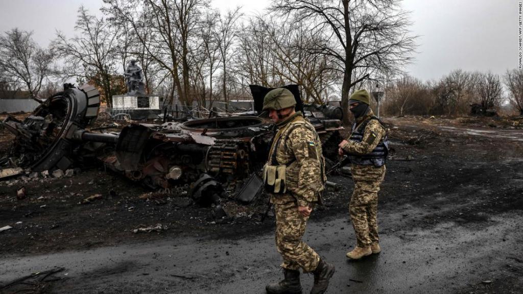 Soldados ucranianos fazem patrulha ao lado de um tanque russo destruído na vila de Lukianivka, perto de Kiev, em 30 de março de 2022.