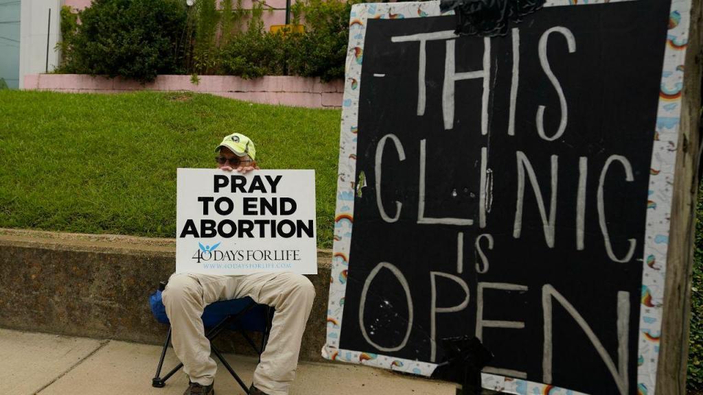Um defensor anti-aborto senta-se atrás de uma placa que informa que a clínica da Jackson Women's Health Organization ainda está aberta em Jackson, Mississippi  (AP Photo/Rogelio V. Solis)