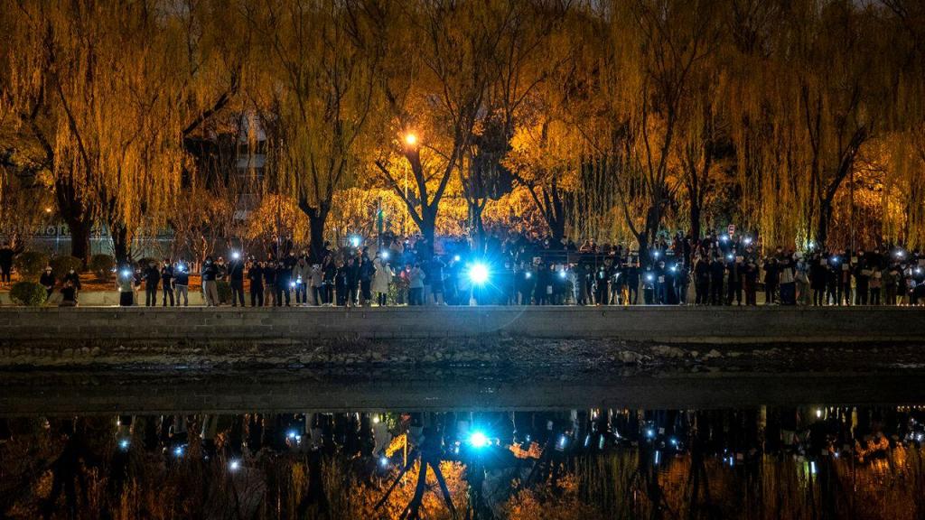 Manifestantes seguram os seus telemóveis durante uma vigília contra as políticas de covid-zero da China, ao longo do rio Liangma, em Pequim, em 27 de novembro de 2022. Créditos: Kevin Frayer/Getty Images