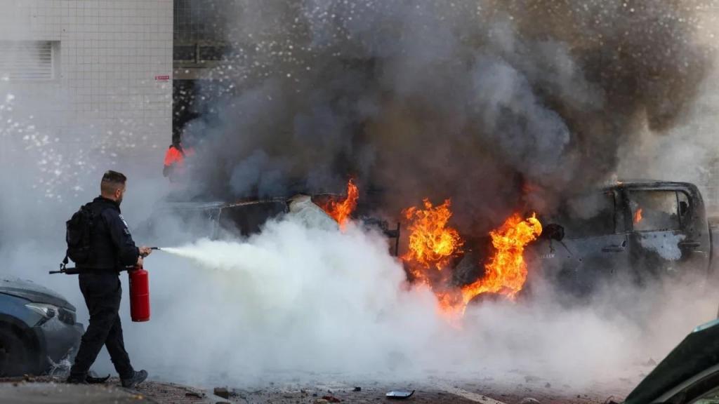 Um membro das forças de segurança israelitas tenta apagar o fogo em carros após um ataque com rockets da Faixa de Gaza em Ashkelon, no sul de Israel. Ahmad Gharabli/AFP/Getty Images