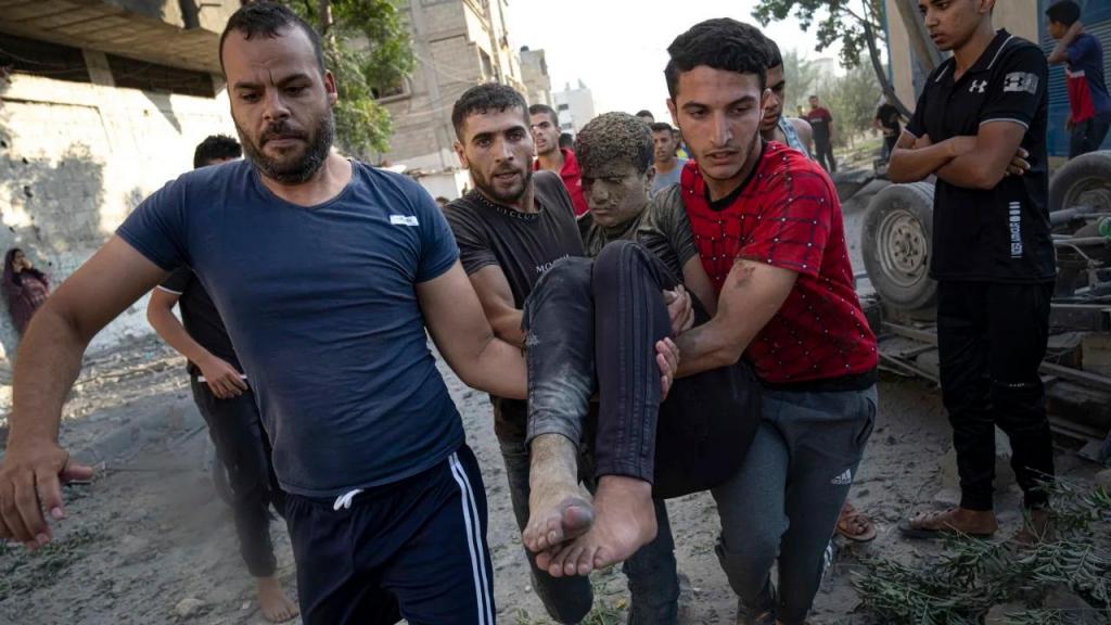 Palestinianos carregam uma pessoa ferida em ataques aéreos israelitas em Khan Younis, Gaza, a 16 de outubro. Fatima Shbair/AP