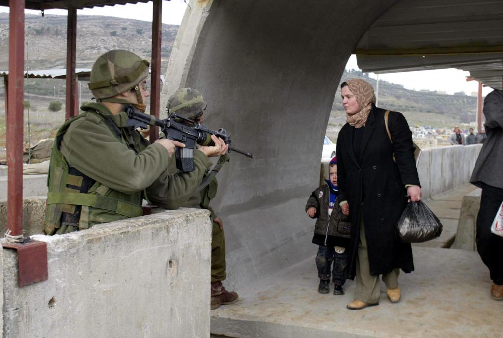 An Israeli soldier aims with his gun as a Palestinian woman and her son cross the West Bank Hawara checkpoint,