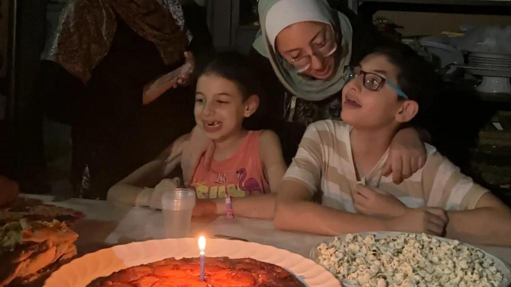 Hashem celebra o seu 12º aniversário com o seu bolo preferido - ananás - ao lado da irmã Basma e da mãe Hiba. Cortesia de Nadia AbuShaban